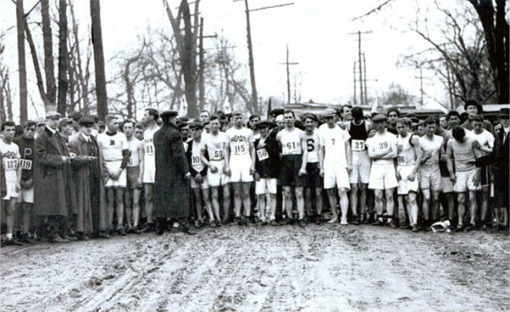 While being given instructions by race organizers, 123 men wait at the starting line of the 1912 marathon on a muddy road among bare trees. © Courtesy of the Ryan Family